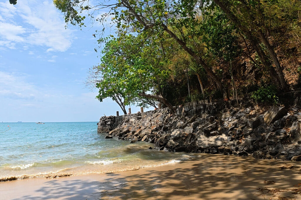 Rocky coastal pathway and lush green trees meeting the sea at Ao Nang Beach, Krabi