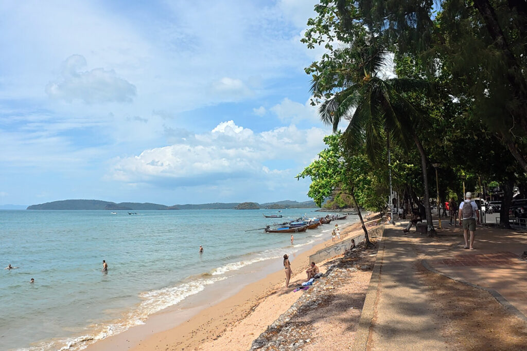 Paved coastal promenade and sunbathers on the sand at Ao Nang Beach, Krabi