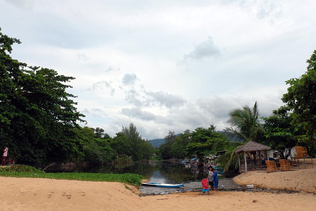 Freshwater mountain stream and canal meeting the beach with moored local boats in Maenam, Koh Samui