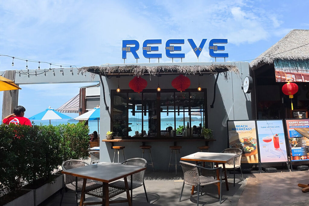 Outdoor dining tables and bar front under thatched umbrellas at Reeve Beach Club, Ao Nang