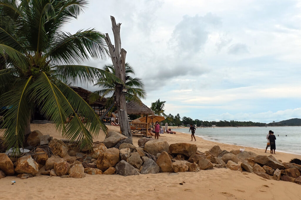 Natural rock barrier and palm trees near a freshwater canal outlet on Maenam Beach Koh Samui