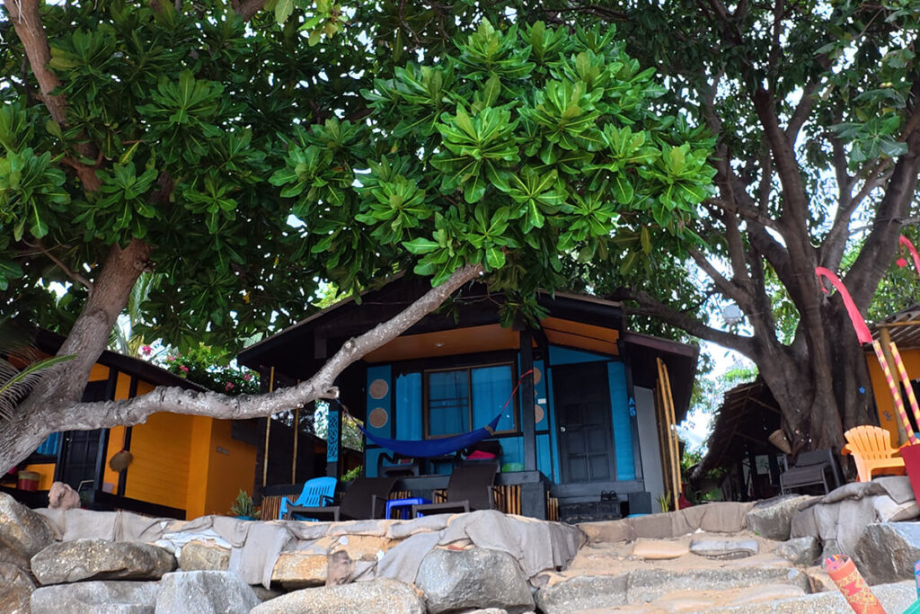 Rustic painted wooden beachfront cabins shaded by large trees at Treehouse Bungalows, Koh Samui