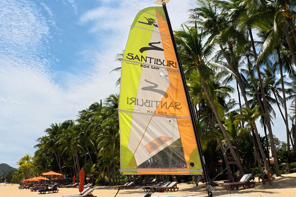 Bright yellow and orange Santiburi sailing catamaran parked on the sand at Maenam Beach