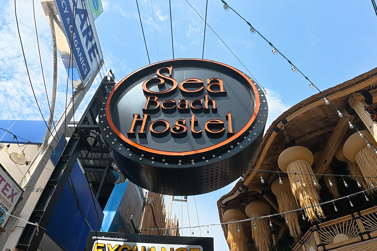 Circular illuminated signboard for Sea Beach Hostel above bamboo-clad boutique entrance in Ao Nang