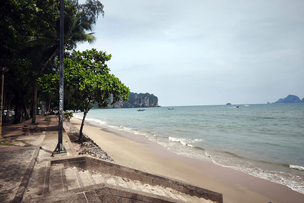 Stone access stairway leading directly onto the sand at Ao Nang Beach with limestone cliffs in the distance